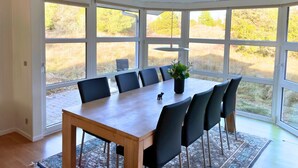 A dining area with a wooden table and chairs, large windows, and a ceiling fan.