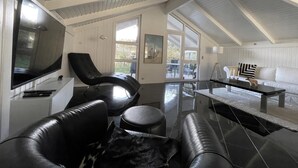 A modern living room with a flat-screen TV, leather sofas, a coffee table, and a dining area with a white table and chairs.