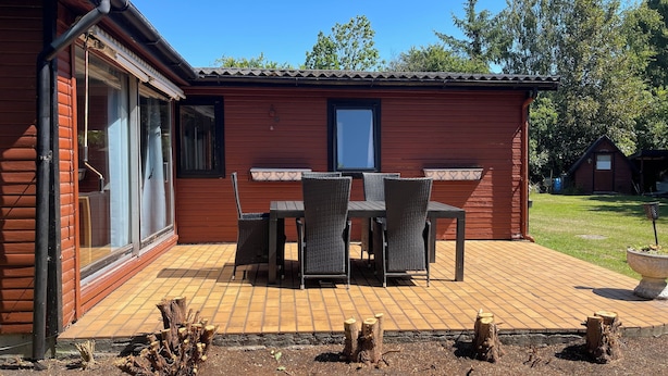 Un edificio in legno con un patio arredato con tavolo e sedie, una finestra e una porta.
