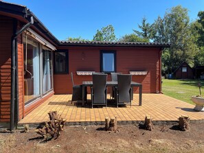 A wooden building with a patio area featuring a table and chairs, a window, and a door. - Charming holiday home in peaceful area (Orø)
