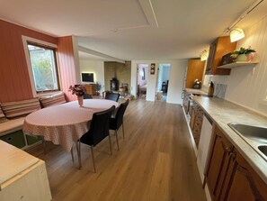 Eine Küche mit Holzschränken, ein Essbereich mit Tisch und Stühlen sowie ein Blick durch eine offene Tür in einen anderen Raum.