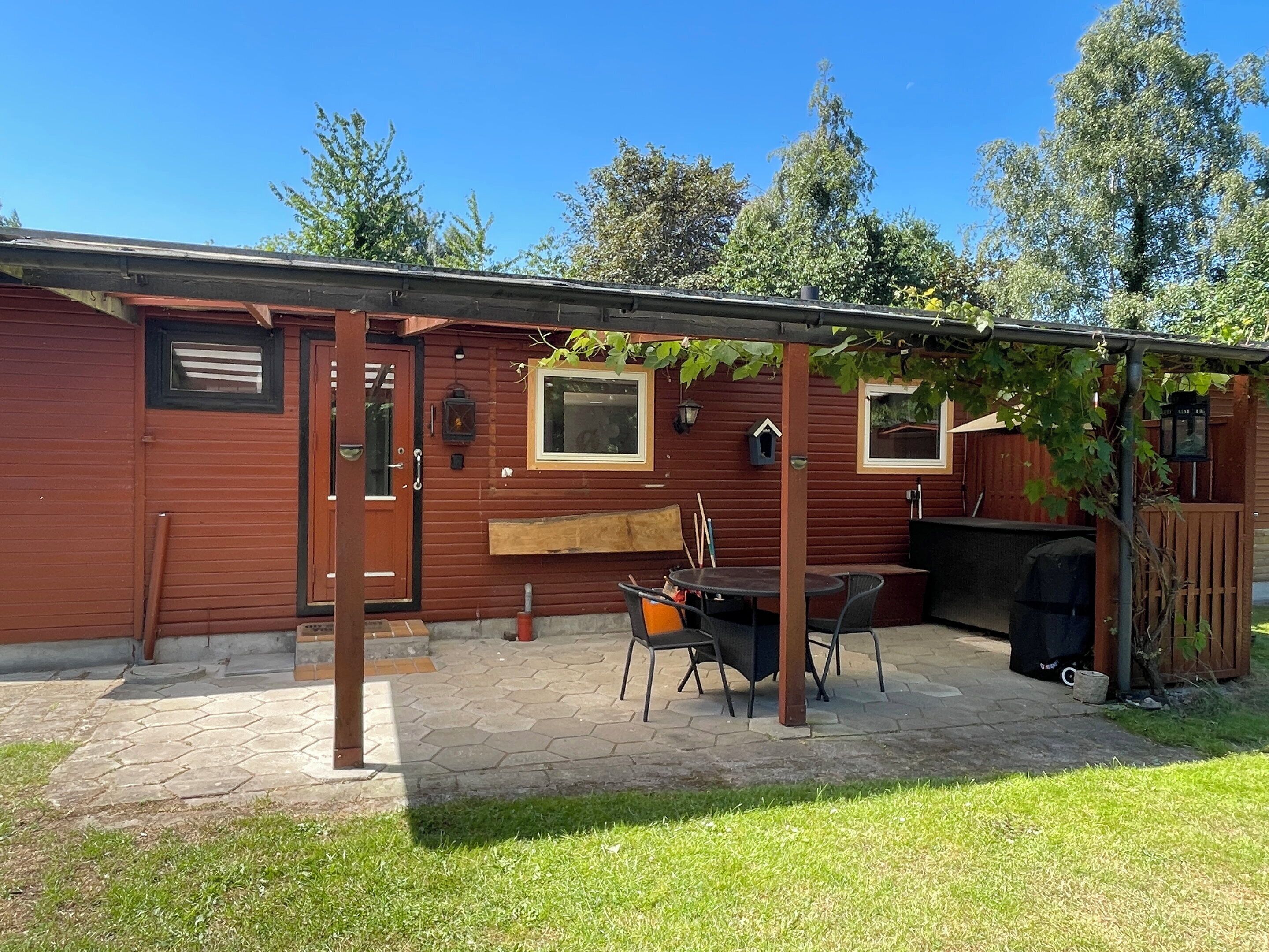 Eine Holzhütte mit einer Terrassenfläche, einem Holztisch und Stühlen.