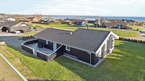 Una casa moderna con una amplia terraza, vistas al mar y un césped bien cuidado.