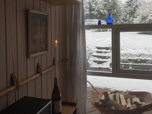 A room with a framed picture on the wall, a candle, a bottle, and a window with a view of snow-covered steps and trees. - Inviting summer house on scenic Røsnæs (Kalundborg)