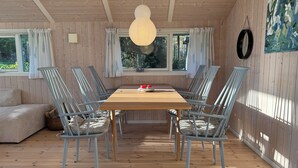 A wooden-paneled room with a wooden table, six chairs, a sofa, and a large window. - Inviting summer house on scenic Røsnæs. (Kalundborg)
