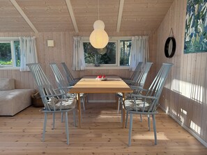Ein Zimmer mit Holzwänden, einem Holztisch, sechs Stühlen, einer Couch und einem großen Fenster.