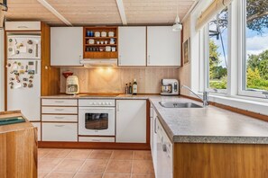 A compact kitchen with a built-in oven, a coffee maker, and a window with a view of greenery. - Inviting summer house on scenic Røsnæs. (Kalundborg)