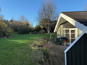 A house with a sloped roof, a front porch, and a clear view of a grassy yard with trees. - Inviting summer house on scenic Røsnæs (Kalundborg)