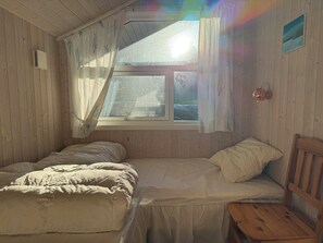 Een kamer met houten wanden, een bed met wit beddengoed, een raam met gordijnen, en een houten stoel.