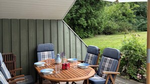 A wooden deck with a round table, blue chairs, and a white umbrella. - Inviting summer house on scenic Røsnæs. (Kalundborg)