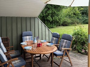 Eine Holzterrasse mit einem runden Tisch, blauen Stühlen und einem weißen Sonnenschirm.