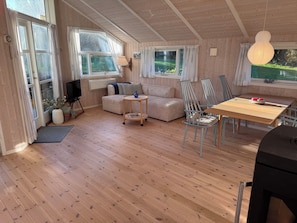 Ein Zimmer mit Holzwänden, einer Couch, einem kleinen runden Tisch, einem Esstisch mit Stühlen und einem Fernseher.