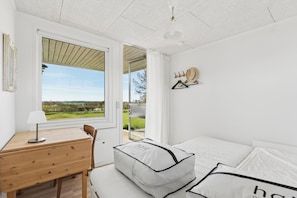 Ein Schlafzimmer mit Bett, Schreibtisch, Stuhl, einem Fenster mit Aussicht und einem Wandhaken für Hüte.