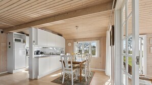 Une cuisine spacieuse avec des meubles blancs, un plafond en bois et un coin repas comprenant une table et des chaises.