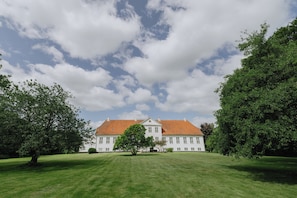A large, white building with a red roof, surrounded by a well-maintained lawn and trees.