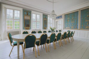 Une salle Ă manger Ă©lĂ©gante, avec une longue table, des chaises Ă revĂȘtement vert et des dĂ©corations murales de style classique.