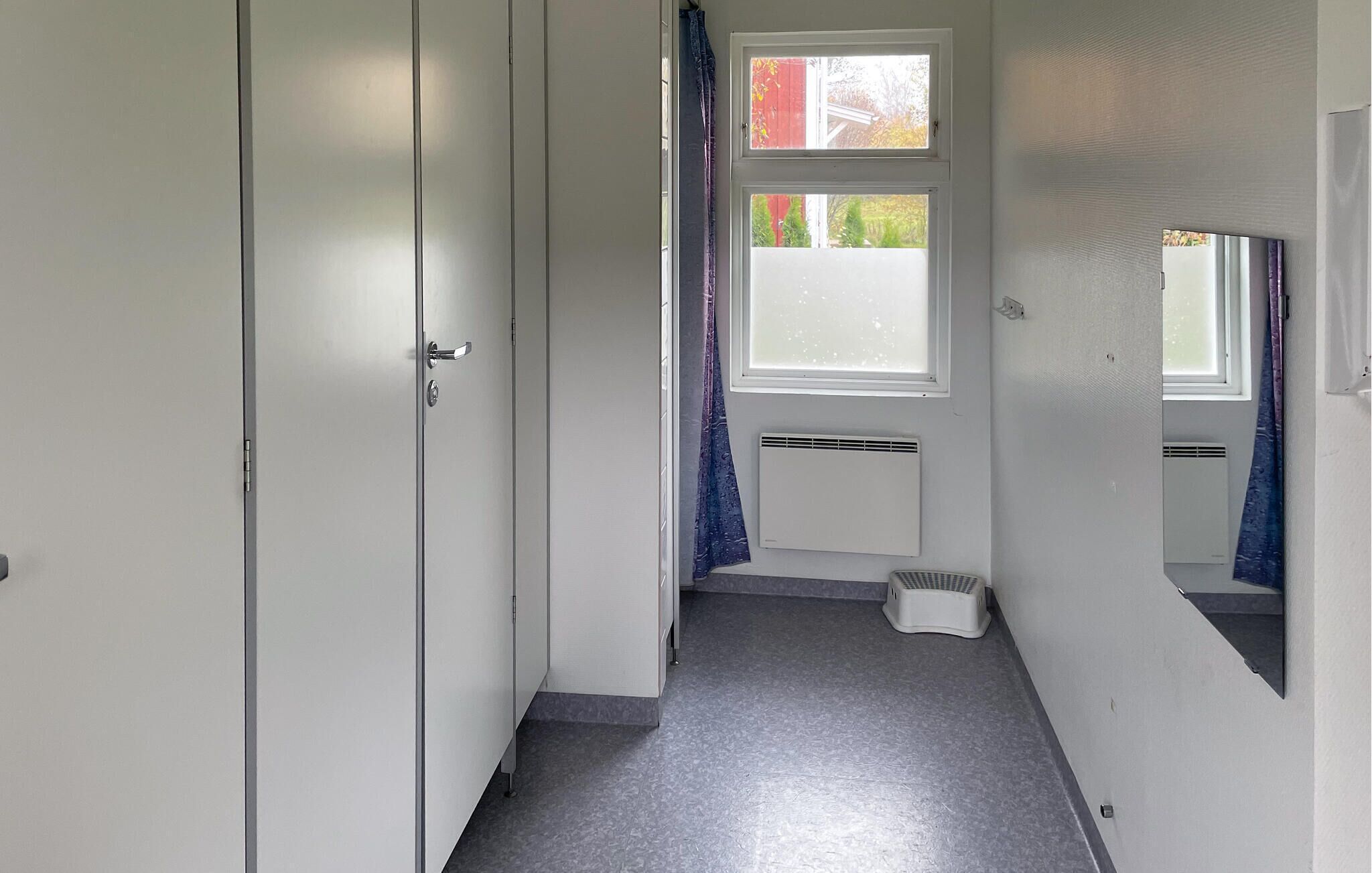 En smal hall med ett fönster, ett element och ett litet trappsteg som leder till en dörr.