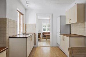 A modern kitchen with white cabinets, a wooden countertop, and a view into a dining area with a brown sofa and table. - Bright modern holiday home near Hindemae (Ullerslev)