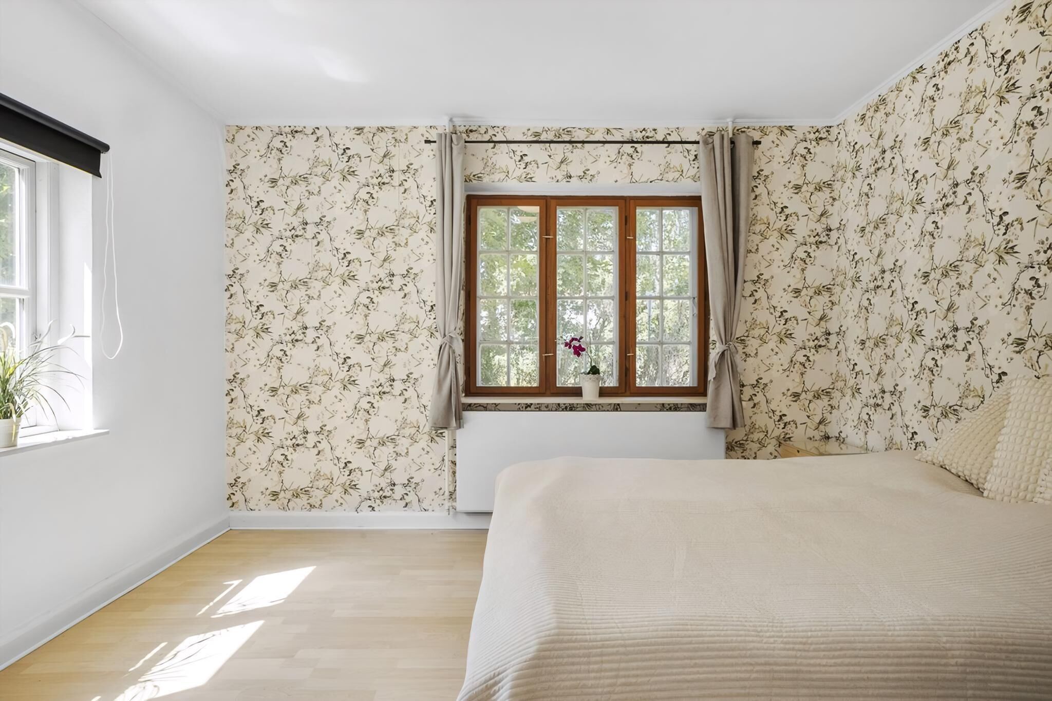 Un dormitorio con una cama, una ventana con cortinas, un radiador y una planta en maceta.