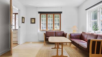 Une pièce avec une table en bois, deux canapés en cuir marron, une fenêtre donnant sur un paysage verdoyant et une porte menant à une autre pièce.
