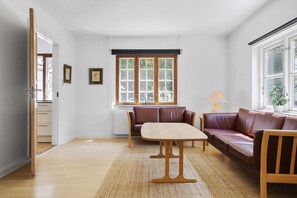 A room with a wooden table, two brown leather sofas, a window with a view of greenery, and a door leading to another room. - Bright modern holiday home near Hindemae (Ullerslev)