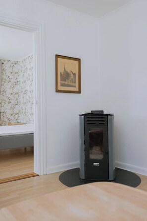 A room with a fireplace, a framed picture on the wall, and a window with floral wallpaper. - Bright modern holiday home near Hindemae (Ullerslev)
