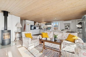 A living room with a sofa set, a coffee table, a fireplace, and a kitchen in the background.