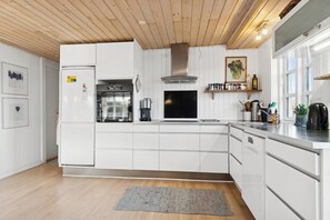 A modern kitchen with white cabinetry, a stainless steel range hood, a built-in oven, and a large window providing natural light. - Classic holiday home near beach and nature (Grenå)