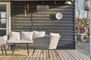 A wooden deck with wicker furniture, a wall-mounted air conditioner, and a decorative plate. - Classic holiday home near beach and nature (Grenå)