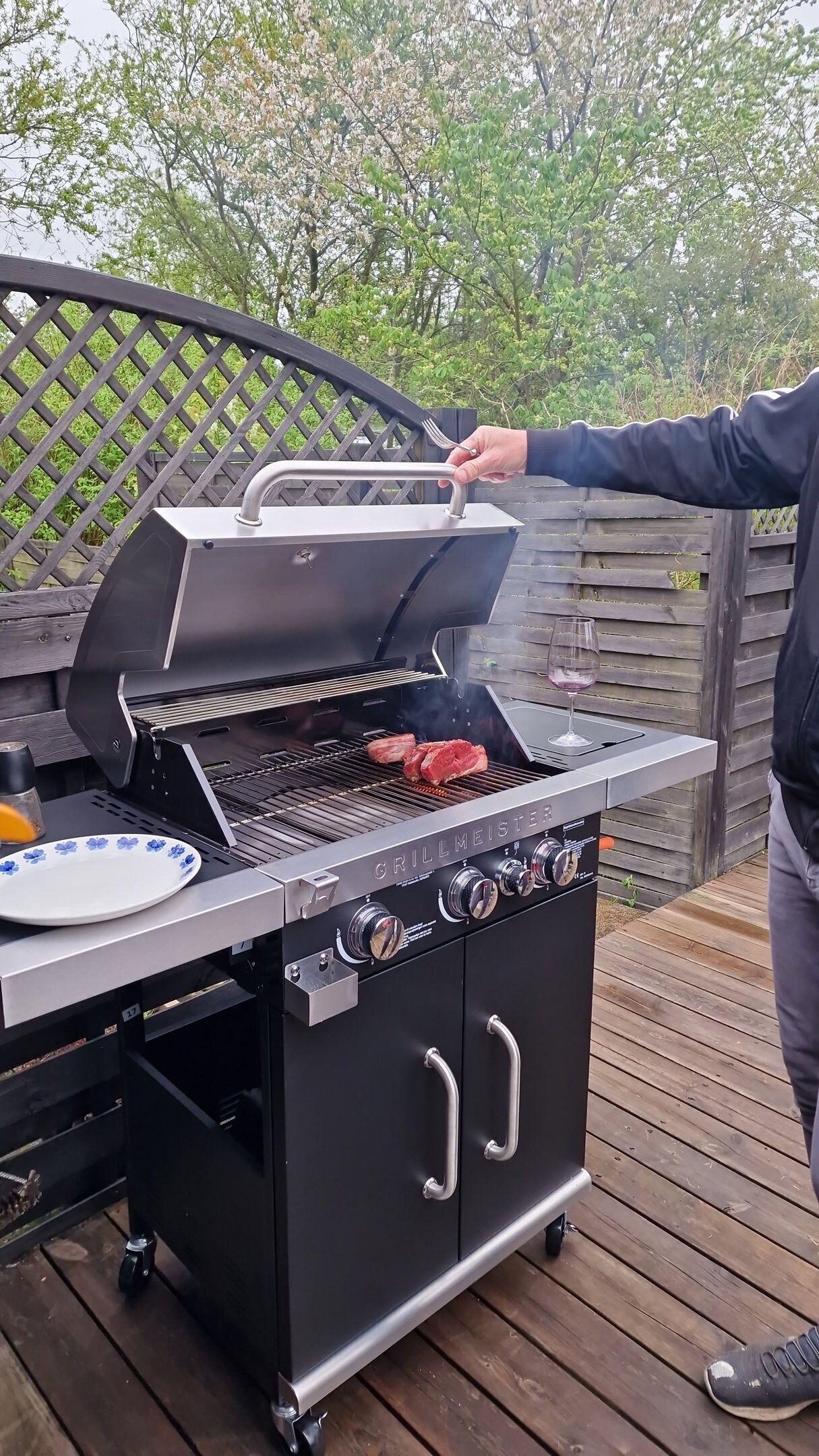Un barbecue portable, avec le couvercle ouvert, laissant apparaître des steaks en train de cuire sur la grille.
