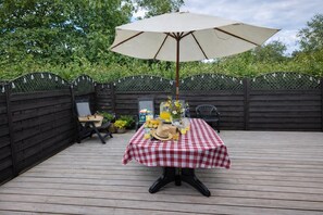 A wooden deck with a checkered tablecloth, a table set with drinks and a hat, and a large umbrella. - Bright Cozy Holiday Home in Hals (Hals)