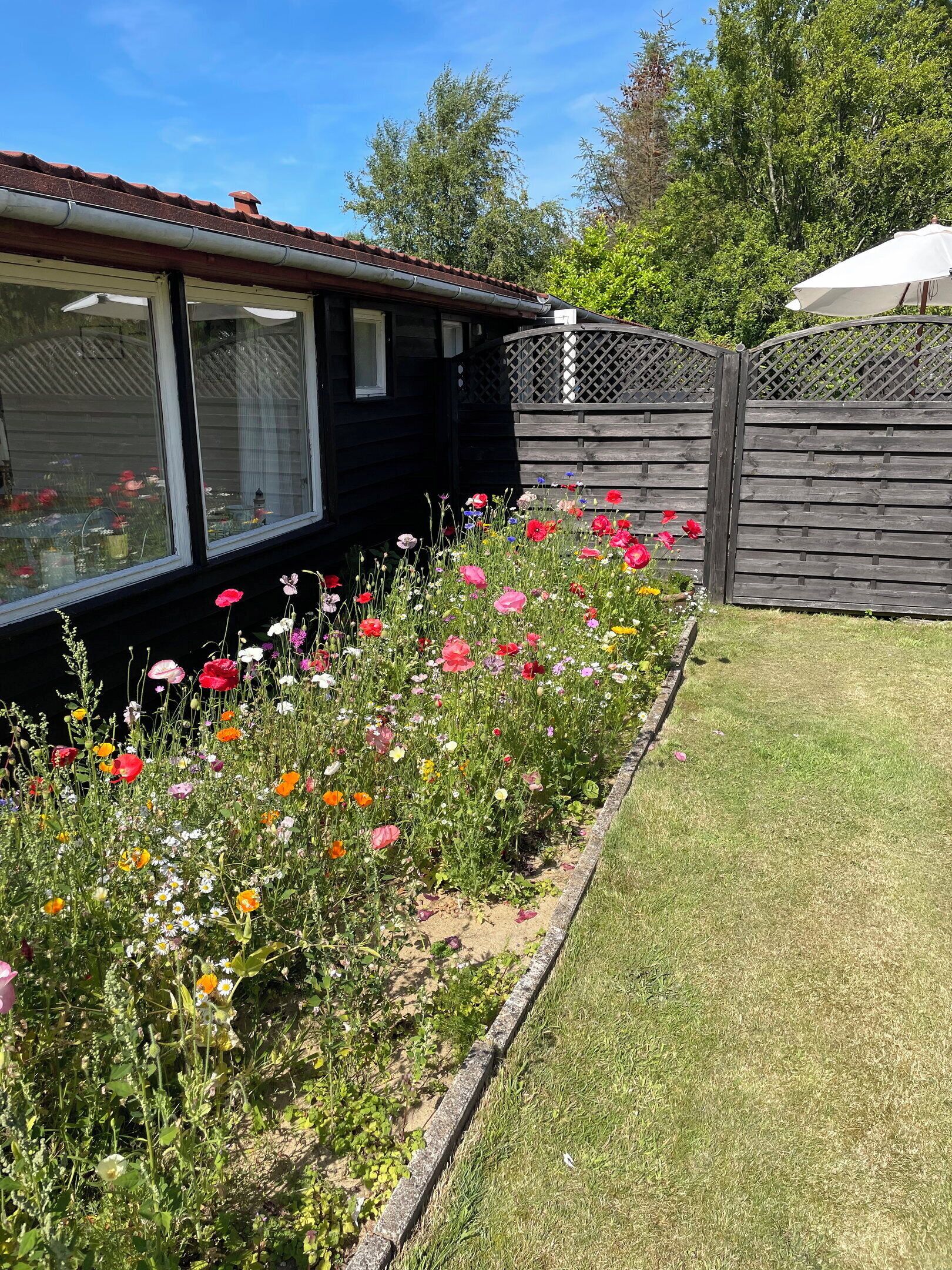 A residential property with a garden bed of various flowers, a wooden fence, and a house with a dark exterior.