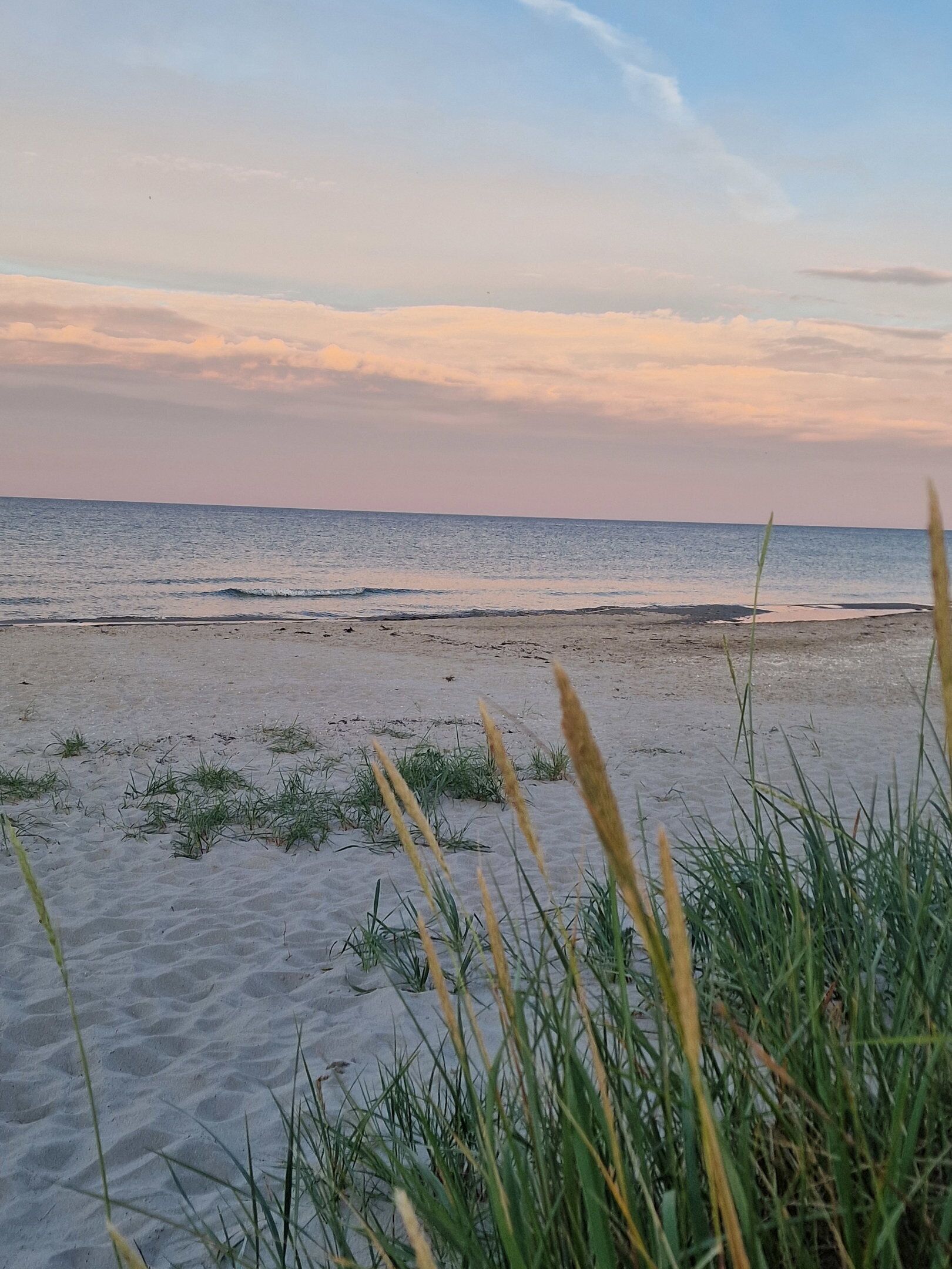 A beach with sand and sparse grass in the foreground.