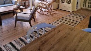 Een gezellige woonkamer met een houten vloer, een bank, een schommelstoel en een eettafel.