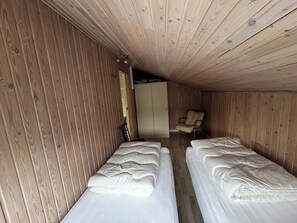 Une petite piĂšce en bois, avec deux lits, une armoire et une chaise.