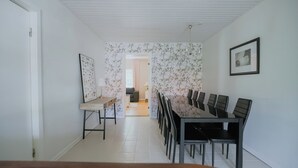 Un espace repas avec une longue table et des chaises, un plafond blanc et une porte sur le côté gauche.