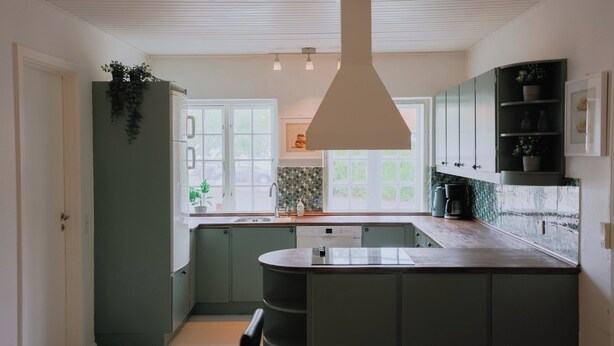 Une cuisine dotée d’un îlot central, de meubles de couleur verte, d’un luminaire suspendu et d’une fenêtre offrant une vue agréable.
