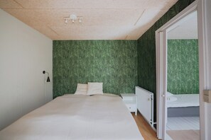 A bedroom with a bed, a nightstand, a white radiator, and a door leading to another room. - Stay in Hindemaes historic managers house (Ullerslev)