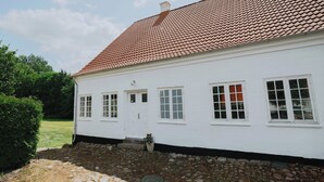 Un bâtiment blanc avec un toit recouvert de tuiles, une porte et des fenêtres.