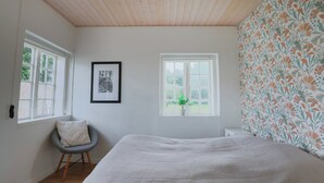 Une chambre à coucher avec un lit, deux fenêtres, une chaise et un tableau encadré accroché au mur.