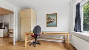 Habitació amb escriptori de fusta, cadira, armari, quadre i finestra amb cortines.