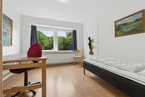 Una habitación con una cama, un escritorio con una silla, una ventana con cortinas y un cuadro en la pared.