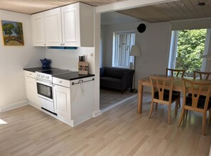 A modern kitchen with white cabinets, a stove, and a black countertop. There is a dining area with wooden chairs and a table. - The coziest farm holiday in the countryside (Tommerup)