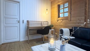 Ett mysigt rum med en väggpanel av trä, ett fönster, en svart lädersoffa, ett litet bord med ett ljus och en stol.