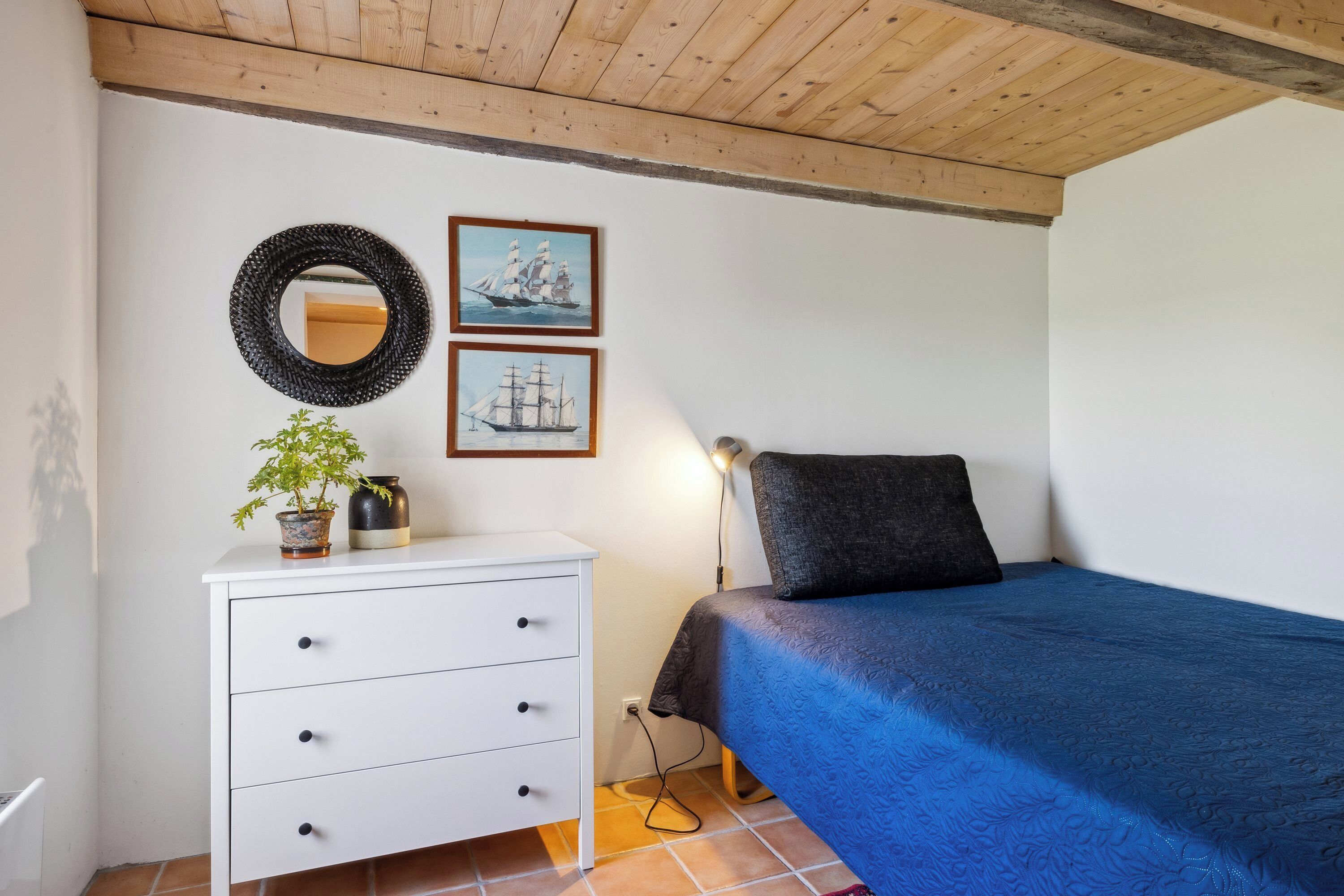 Ein Schlafzimmer mit einem Bett, einer weißen Kommode mit Schubladen, einem Spiegel und zwei gerahmten Bildern an der Wand.
