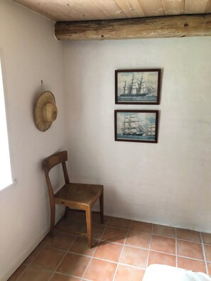 A room with a wooden chair, a wall-mounted hat, and two framed paintings of sailing ships.