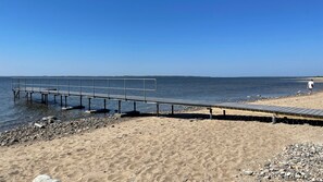 A beach with a wooden pier extending into calm waters, a sandy shore, and a clear sky. - Enjoy the silence and stunning view over the sea (Spøttrup)