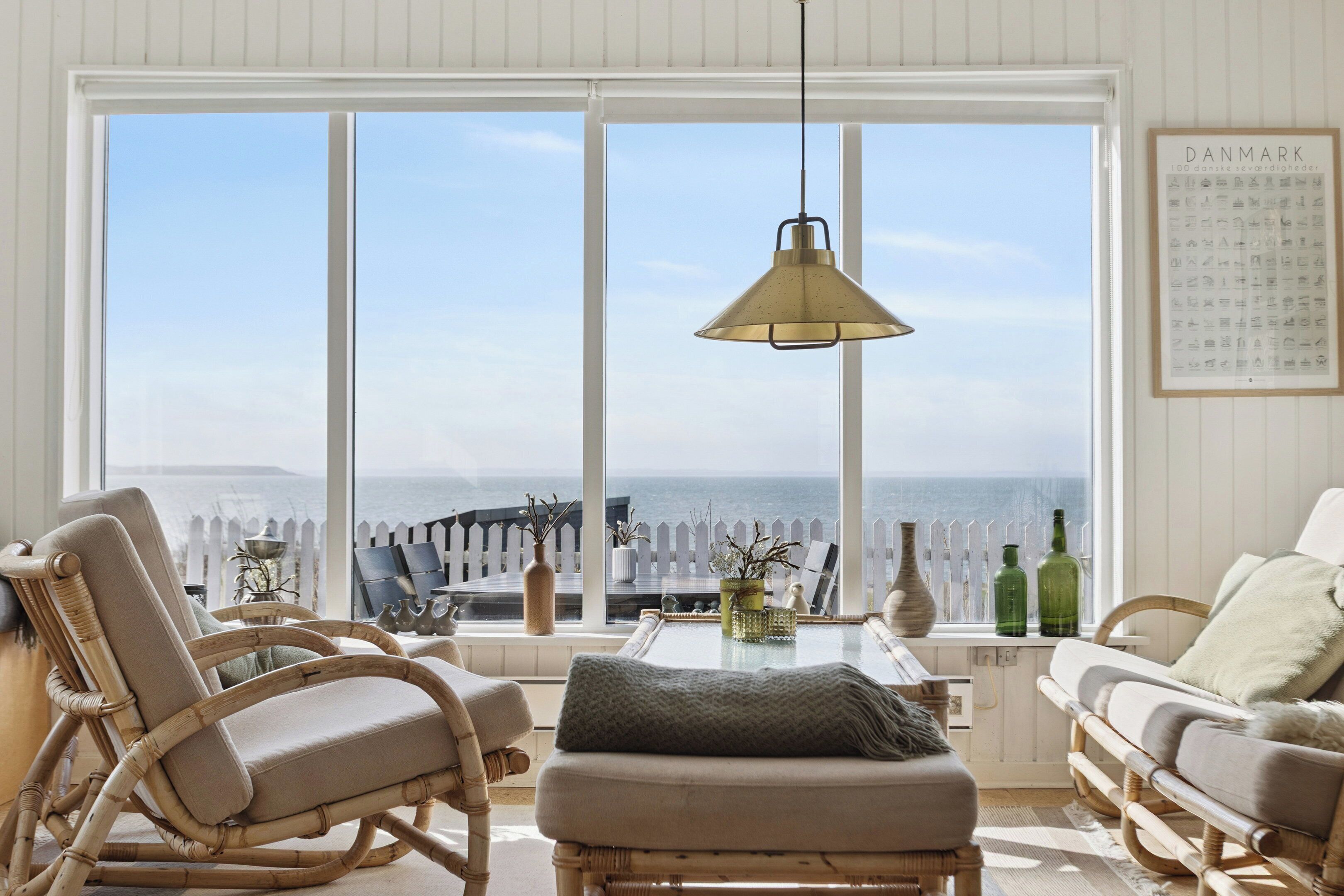 A room with a large window, wicker furniture, a hanging lamp, and a framed map on the wall.