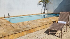 A swimming pool with a stone border, a lounge chair, and a palm tree. - Friendly En-suite, to relax after a day of work / studies. (São Paulo)