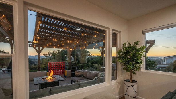 Un espacio de sala acogedor con un ventanal grande que da a un patio con una chimenea y luces colgantes.